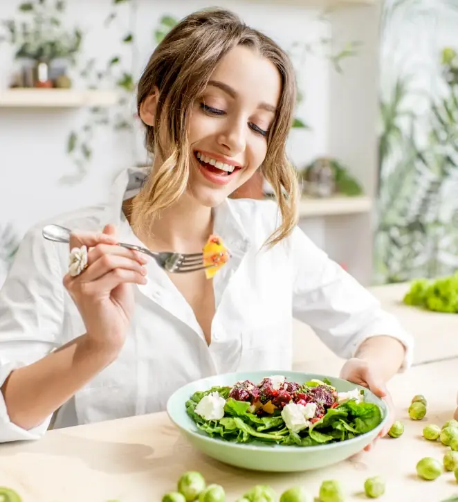 A woman eating a fresh green salad in a bright kitchen