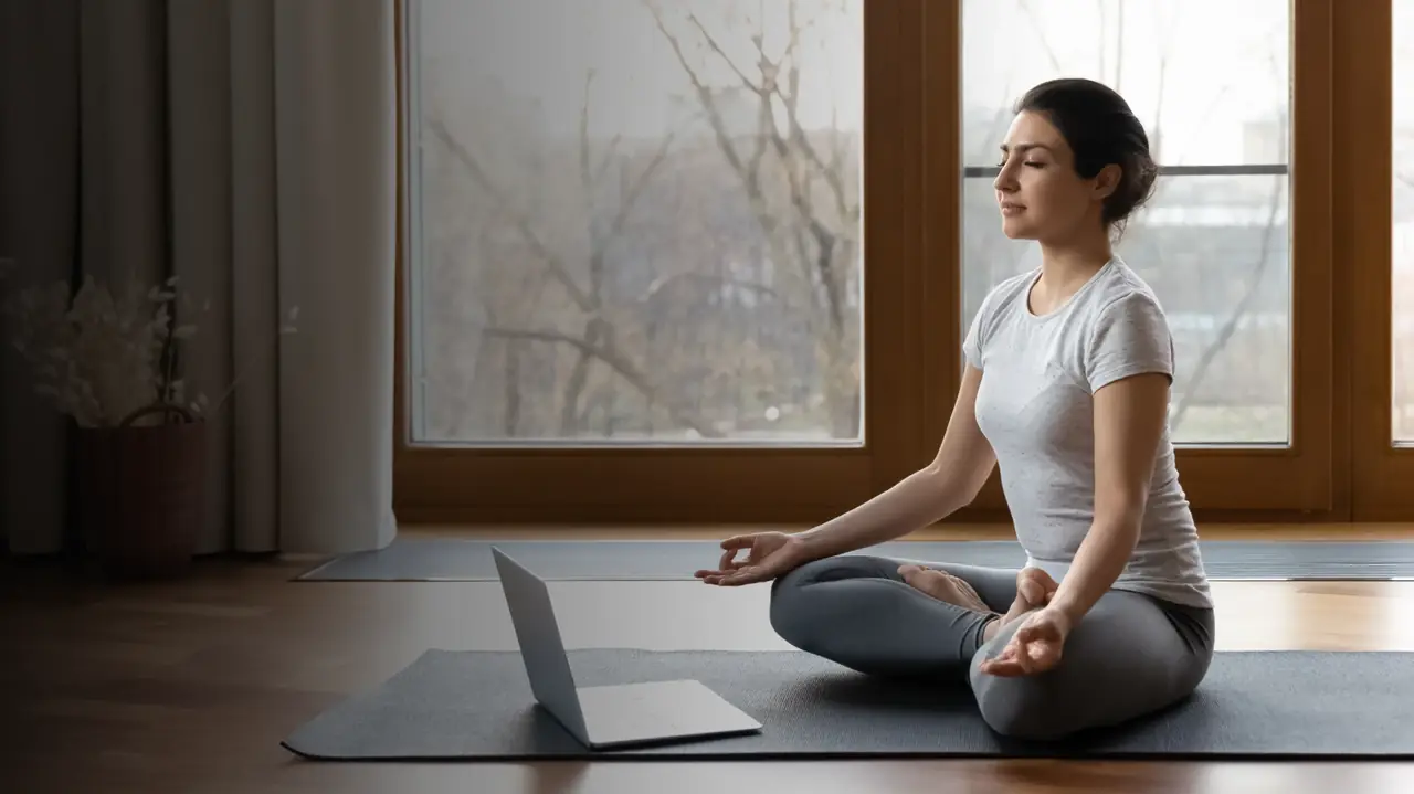 A woman following an online yoga session from a laptop at home