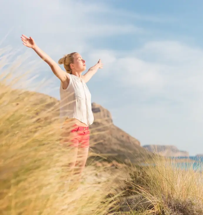 A woman standing in tall grass with her arms open to the sky
